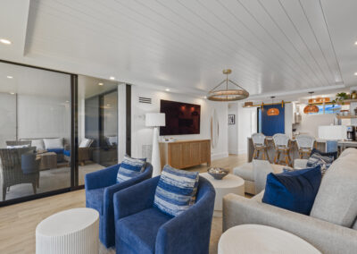 Bright modern living room with off-white sectional and blue chairs - large wall-mounted TV and floor to ceiling windows