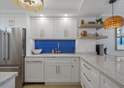 Post-remodel: bright and light modern kitchen with white cabinets, gold hardware, blue tile backsplash, and stainless fridge