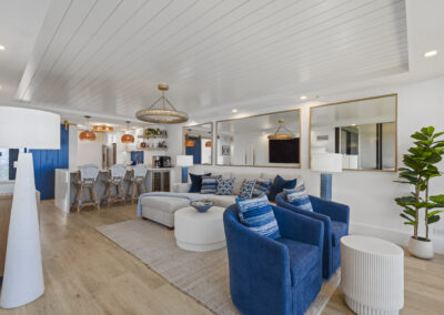 Bright modern living room with off-white sectional and blue chairs - large wall-mounted TV and floor to ceiling windows
