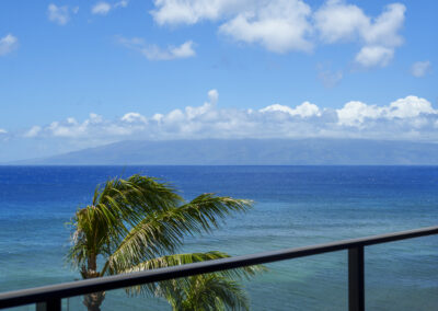 Bright blue sweeping ocean view with outer island of Molokaiin distance and palm tree leaves in waving with breeze.