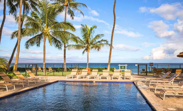 The Mahana poolside view of sunchairs and bright blue pool water overlooking ocean
