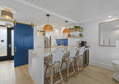Post-remodel: breakfast bar area with tall chairs by kitchen and large blue barndoor open showing entryway