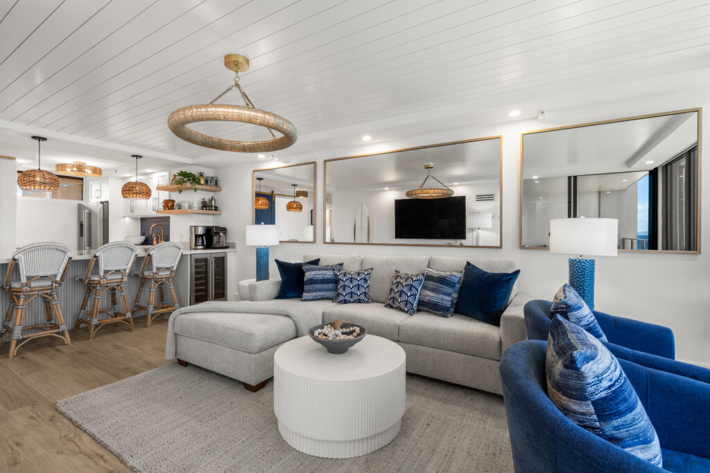 Bright modern living room with off-white sectional and blue chairs and mirrored back wall