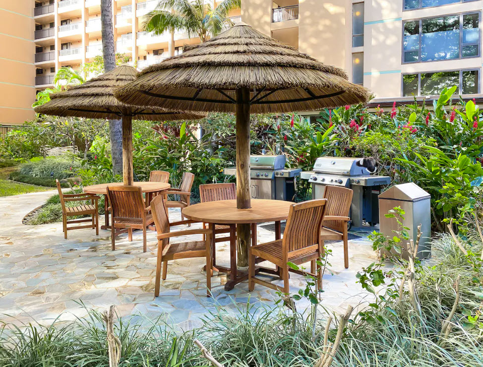 Outdoor eating area with sunchairs, umbrellas, and BBQ grills.
