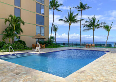 The Mahana poolside view of sunchairs and bright blue pool water overlooking ocean