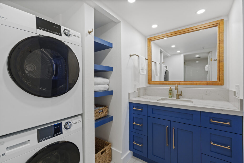White washer and dryer frontloading stack in bathroom with bright blue vanity